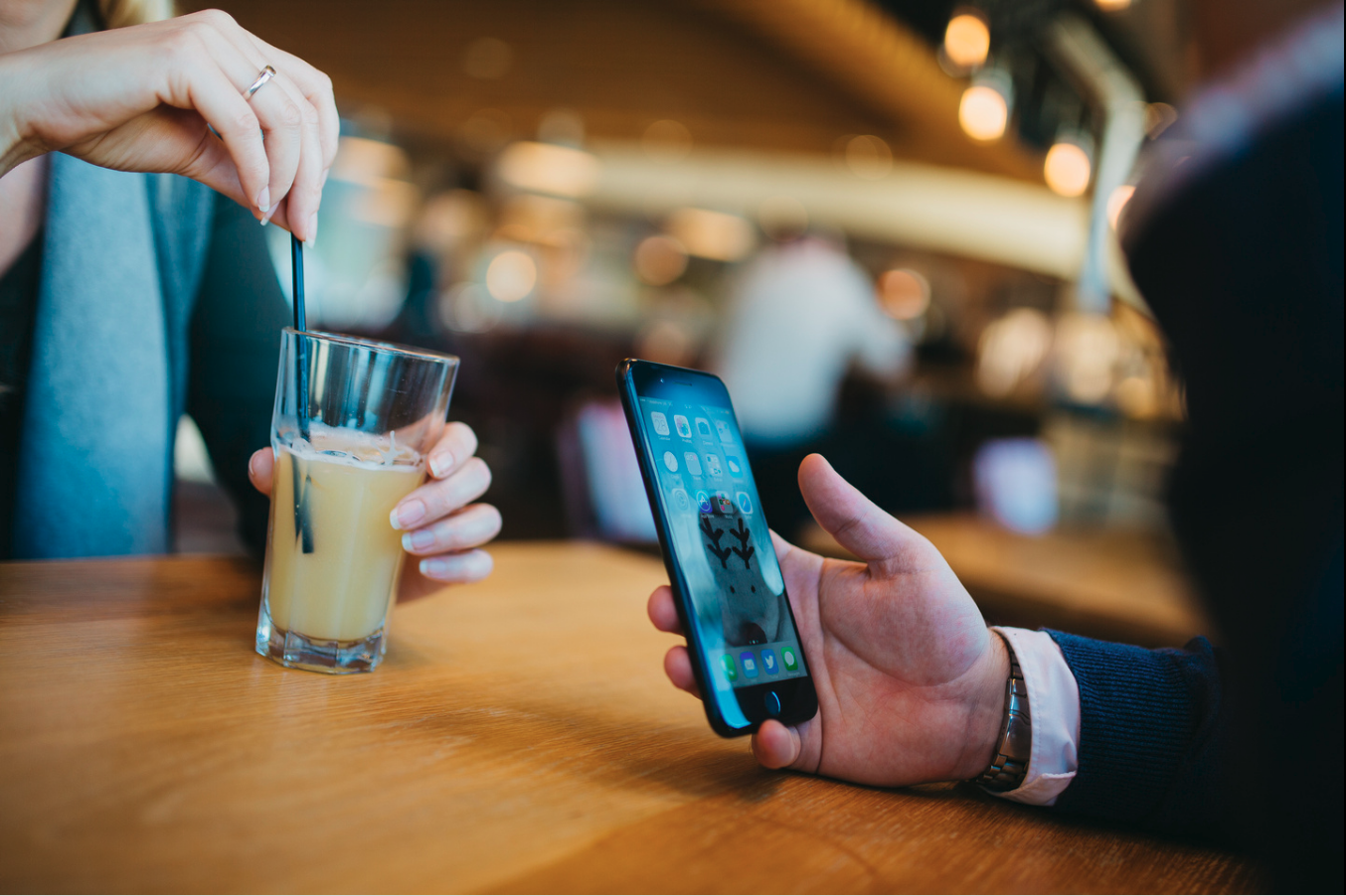 A man holding a mobile phone sat opposite a woman holding a drink